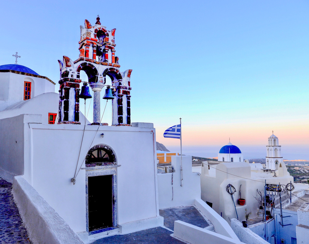 Kirke med bjeller som klokker og utsikt ved soloppgang i Pyrgos Santorini.