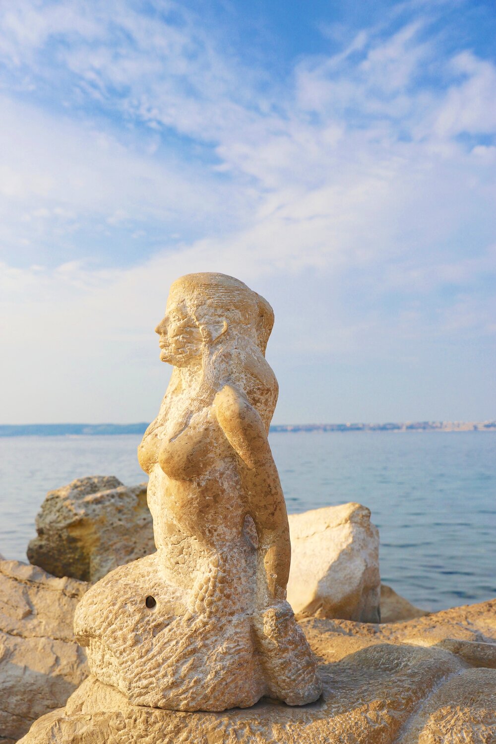 Statue ved havet en havfrue som speider utover.