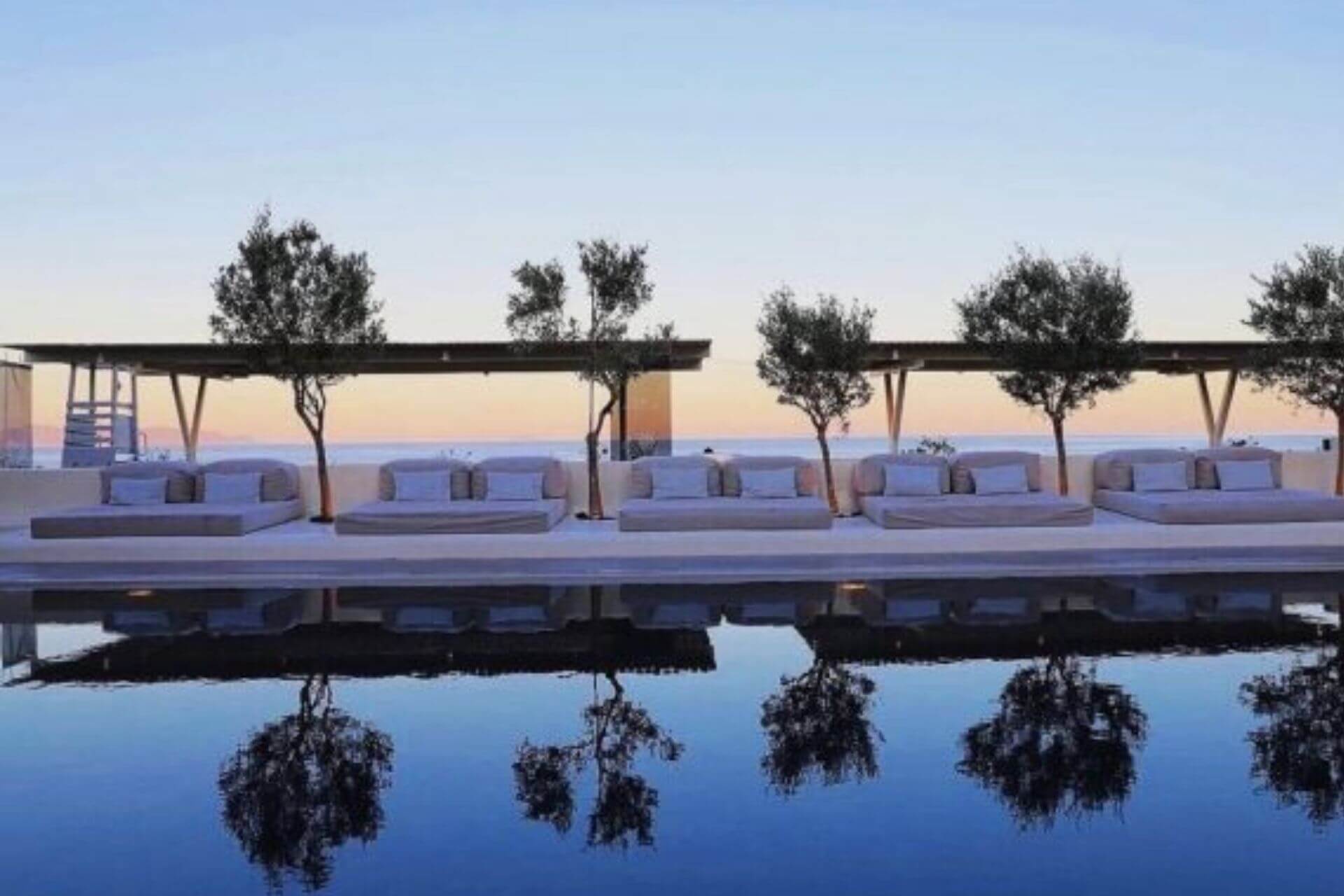 Basseng med loungem&oslash;bler og oliventr&aelig;r i solnedgang ved Bellonias Villas i Kamari p&aring; Santorini