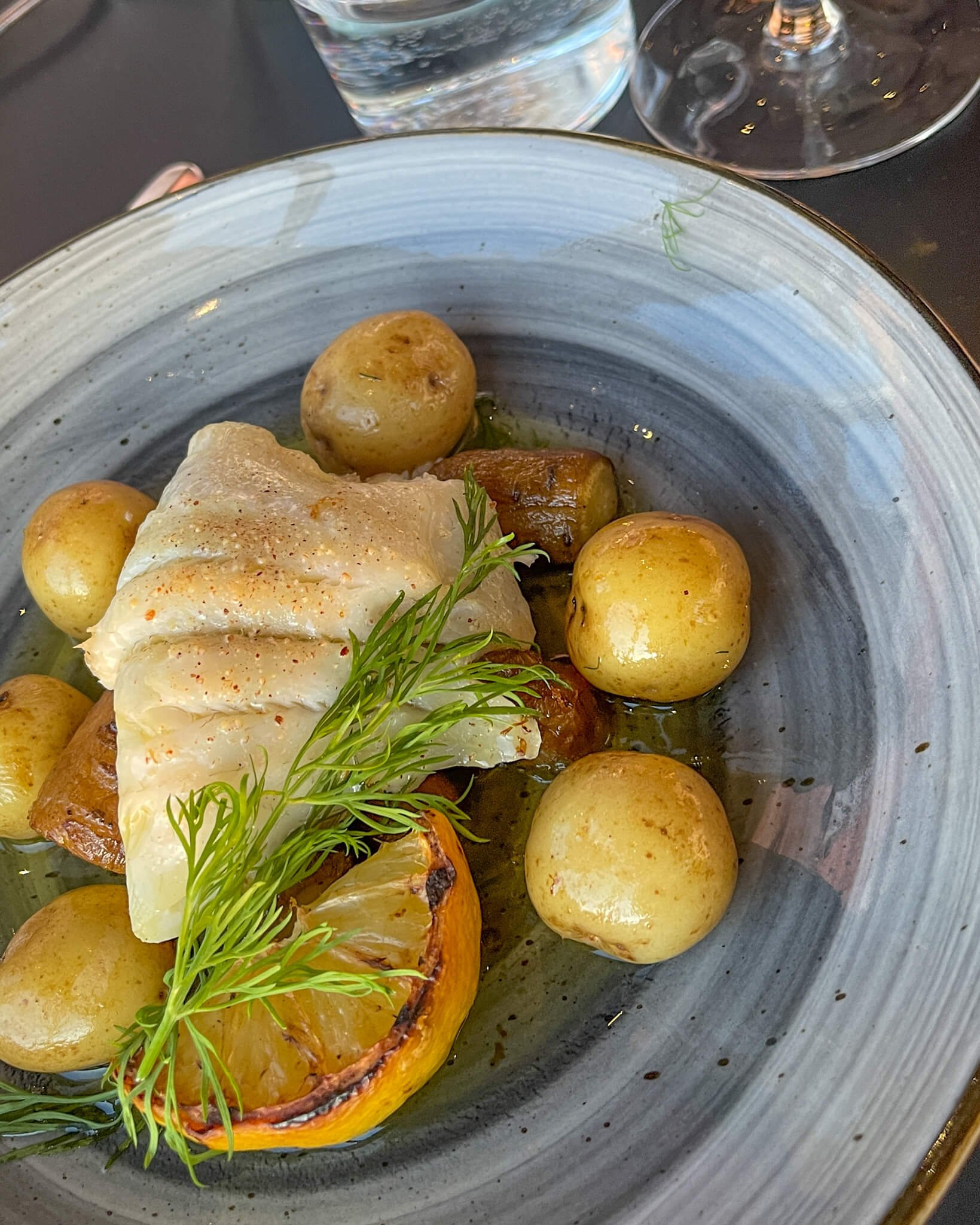 Fersk fisk med grønnsaker og små poteter servert på blå og lekker tallerken i restauranten. 