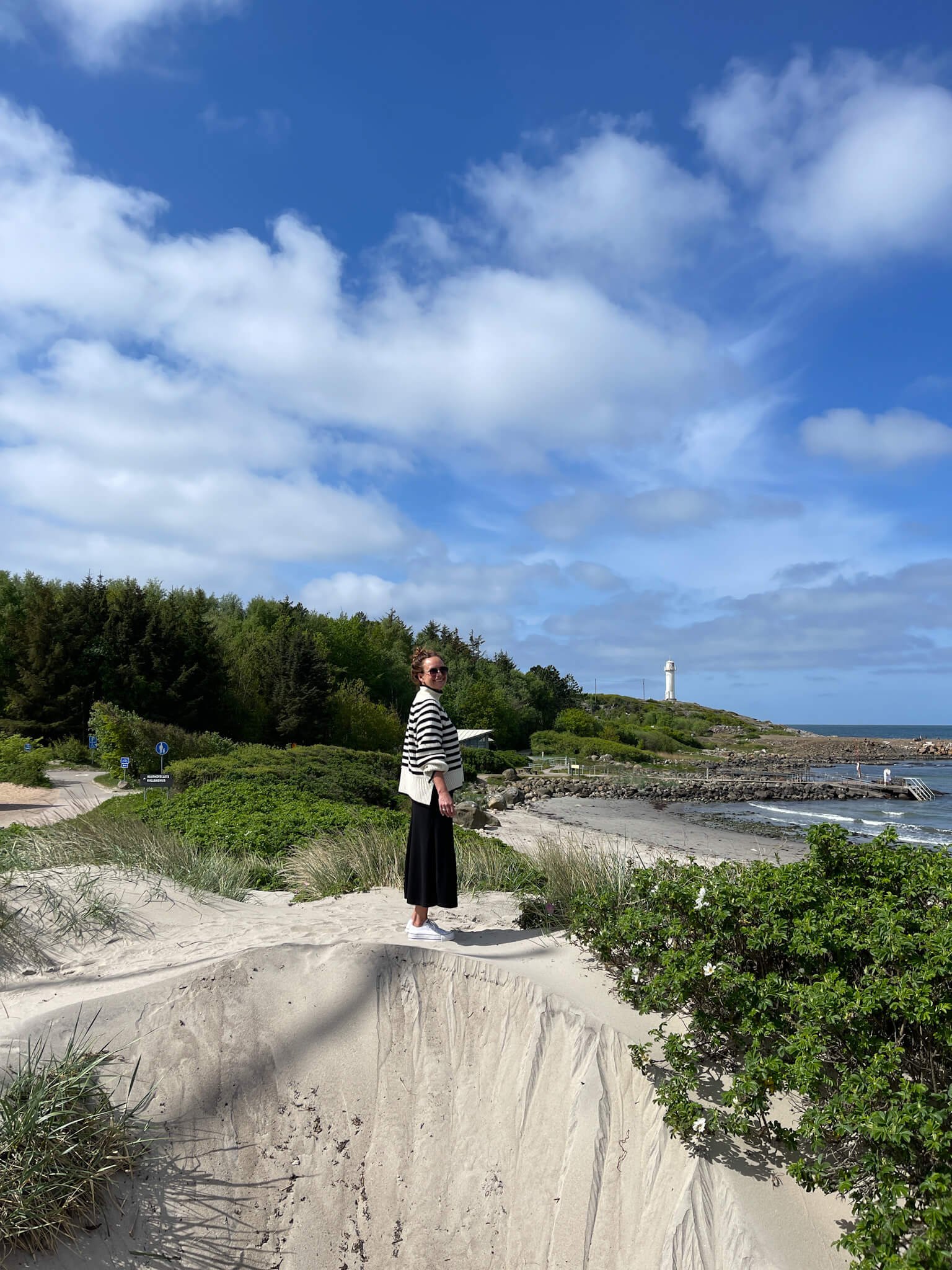 Dame i maritim hvit og blåstripete genser på stranden i Lilla Apelviken med Subbe fyr i bakgrunnen. 