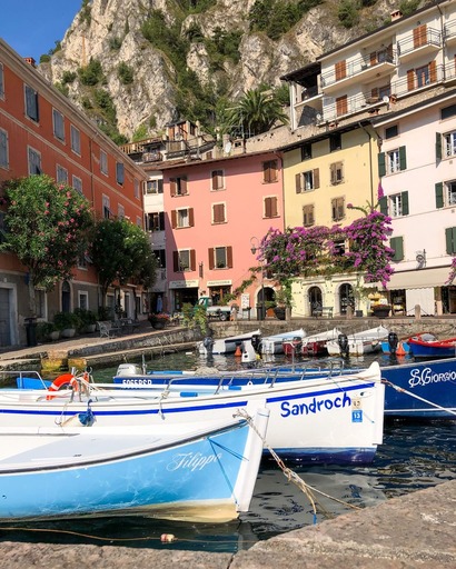 Små ikoniske båter i havnen i Limone sul Garda. Bak fargerike bygg i pastell.