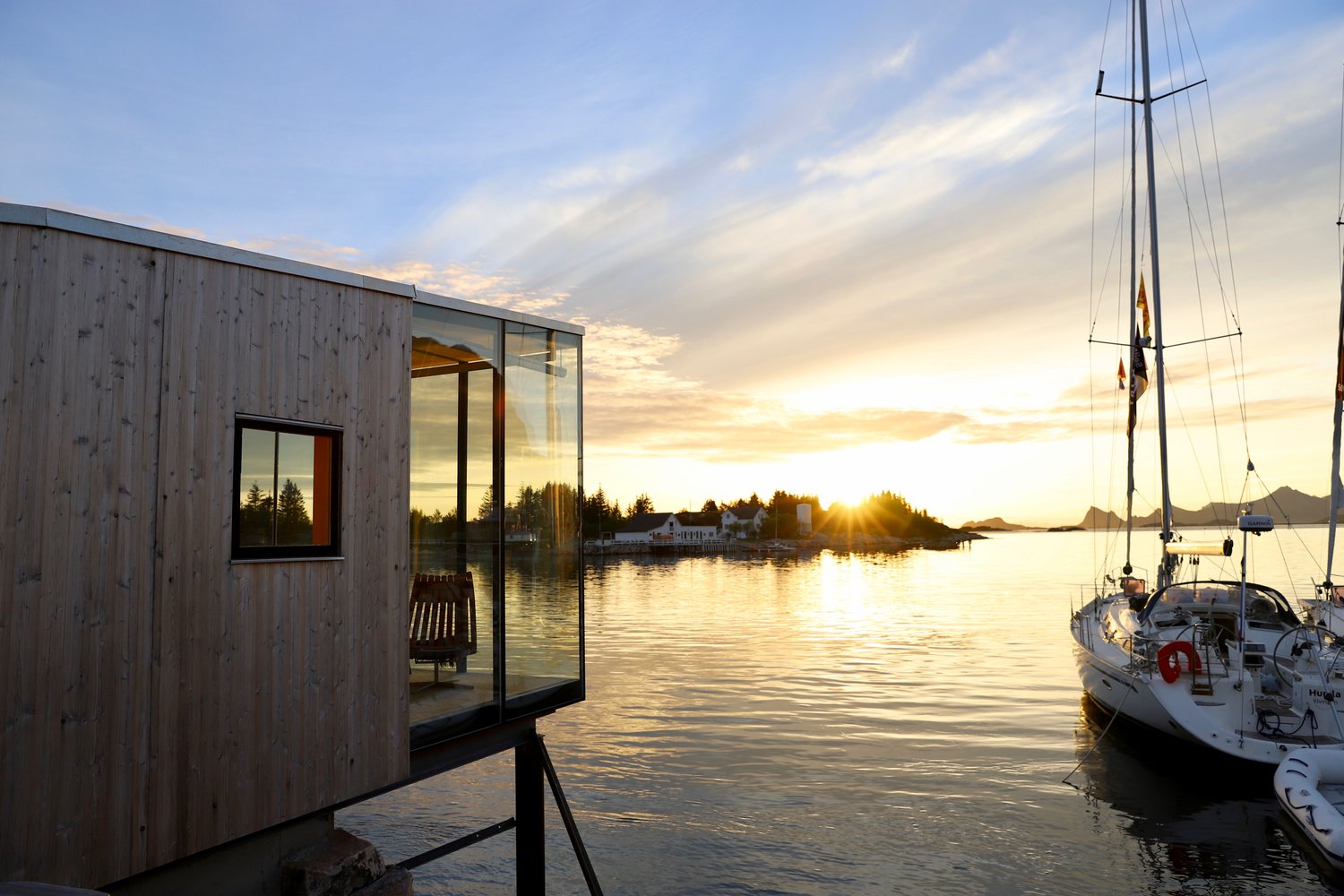 Sjøhytte på Manshausen i midnattsol med seilbåter fortøyd ved bryggen. 