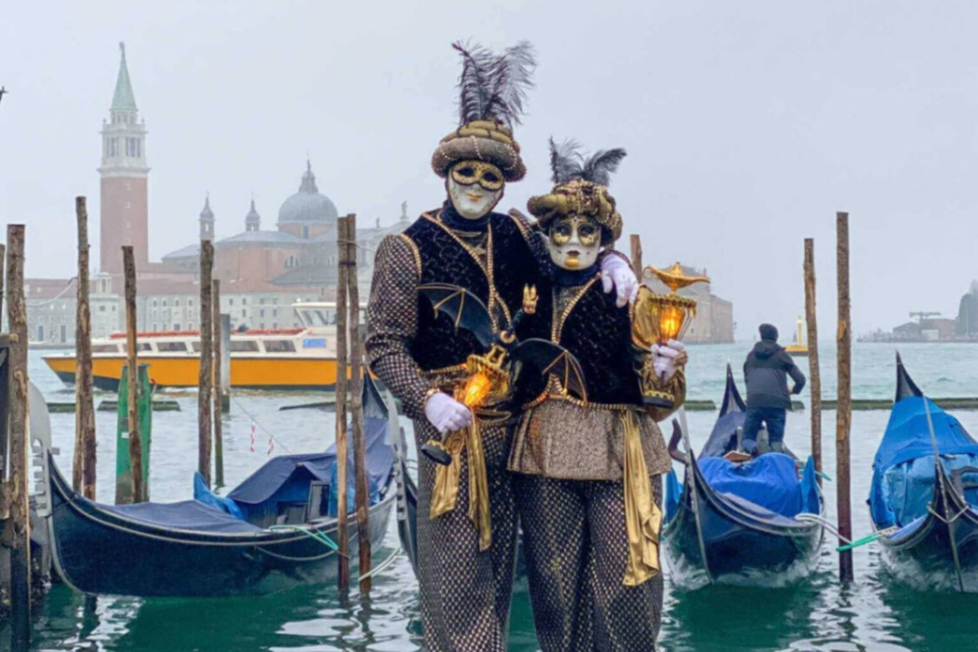 To personer i masker under karnevalet i Venezia med gondoler i bakgrunnen.