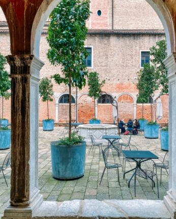 Rimelig overnatting i Venezia. Hostell med hyggelig bakgård med planter, bord og stoler.