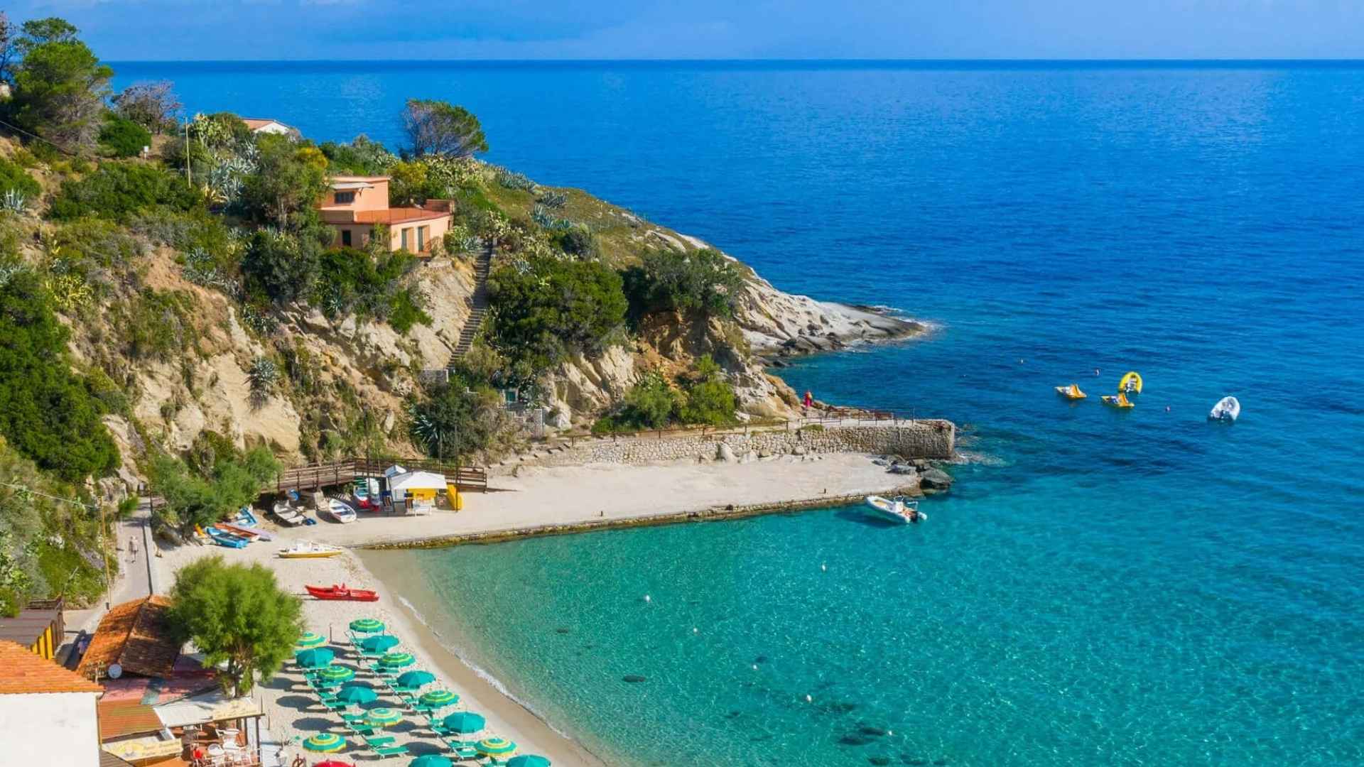 Sandstrand med solsenger, parasoller, og turkist hav på Elba. 