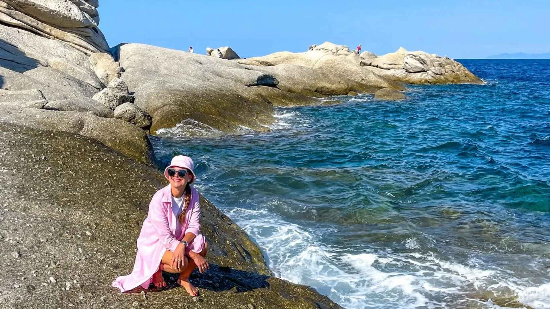 Reiseblogger Merete Moen i rosa på klippene ved havet på Elba. 