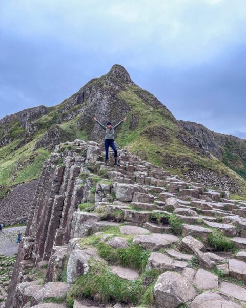 Dame med lue, støvler og jakke men hendene i været ved Giant´s Causeway i Nord Irland.