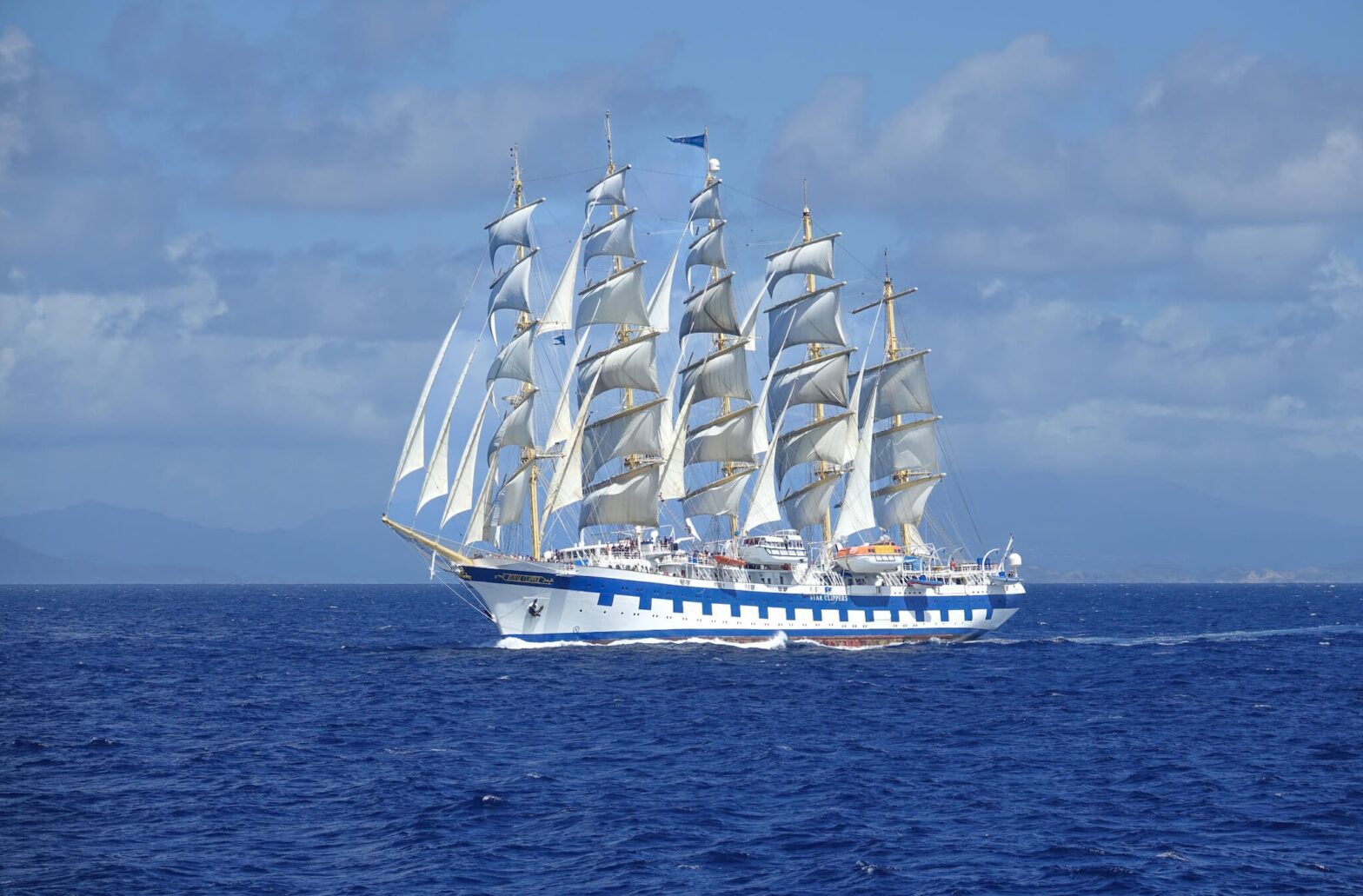 Royal Clipper for fulle seil på blått hav med blå himmel.