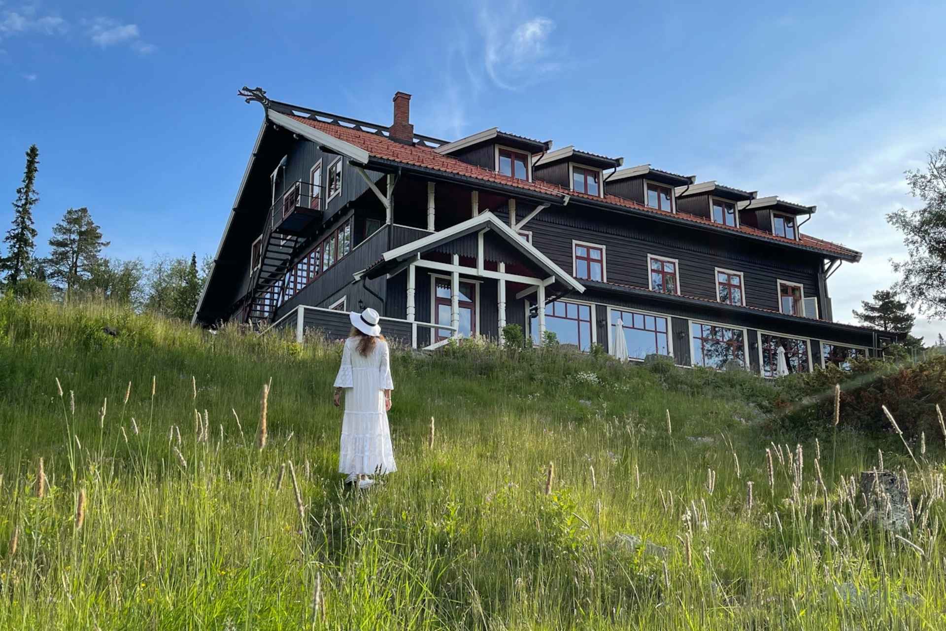 Tuddal H&oslash;yfjellshotell i Telemark omgitt av sommereng og dame i hvit kjole. 