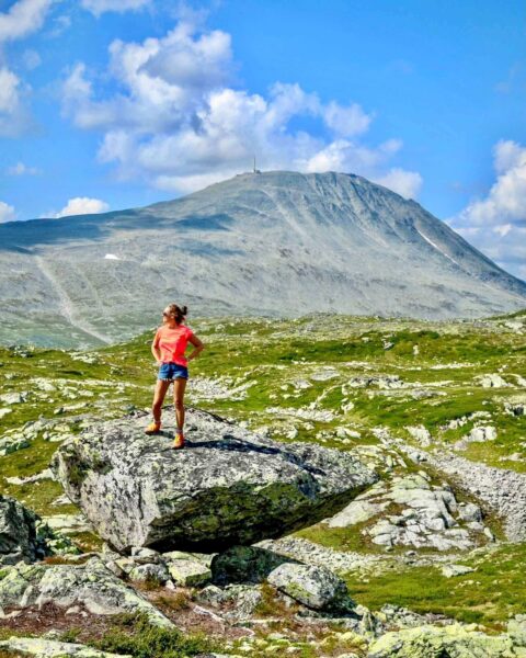 Dame i sommerklær og fjellsko på fjelltur. Gaustatoppen i bakgrunnen. Det er fint vær, blå himmel og varmt.