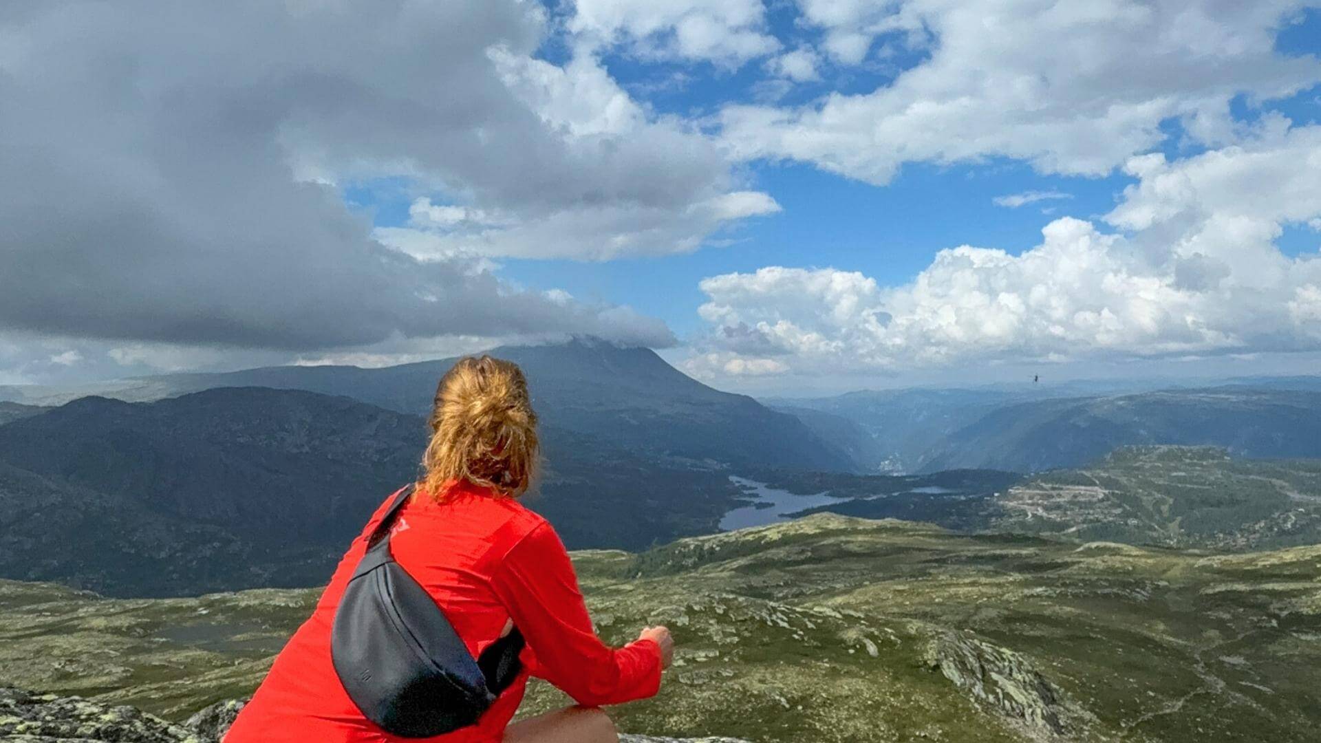 Utsikt til Gaustatoppen. I forgrunnen en dame kledd i røde turklær. 