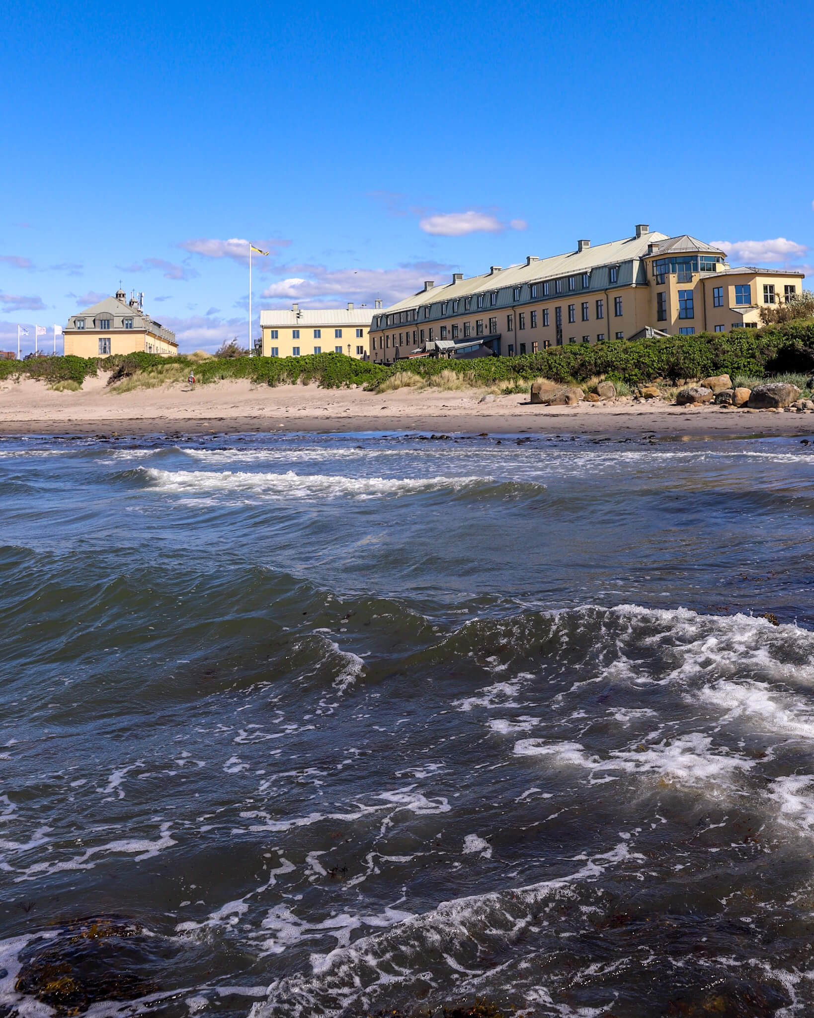 Varbergs Kusthotell sett fra havet. I forgrunnen bølger som slår mot land og den fine sandstranden foran hotellet. 