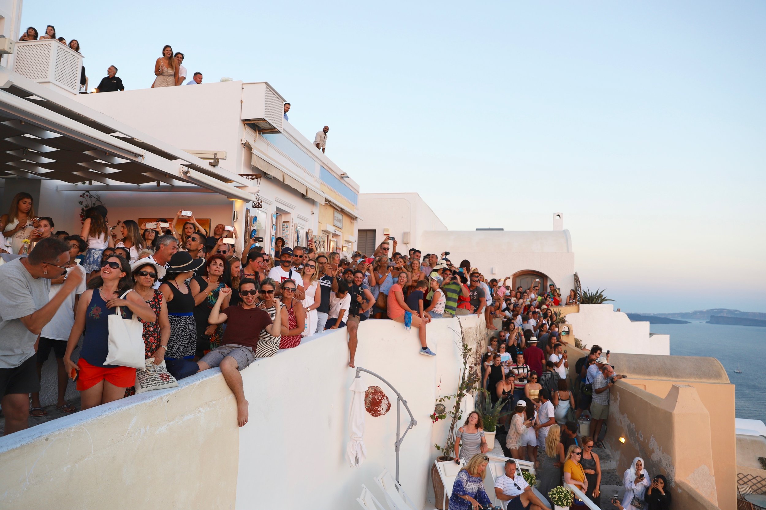 Store folk folkemengder har samlet seg og venter på å se solnedgangen på Oia på Santorini. 