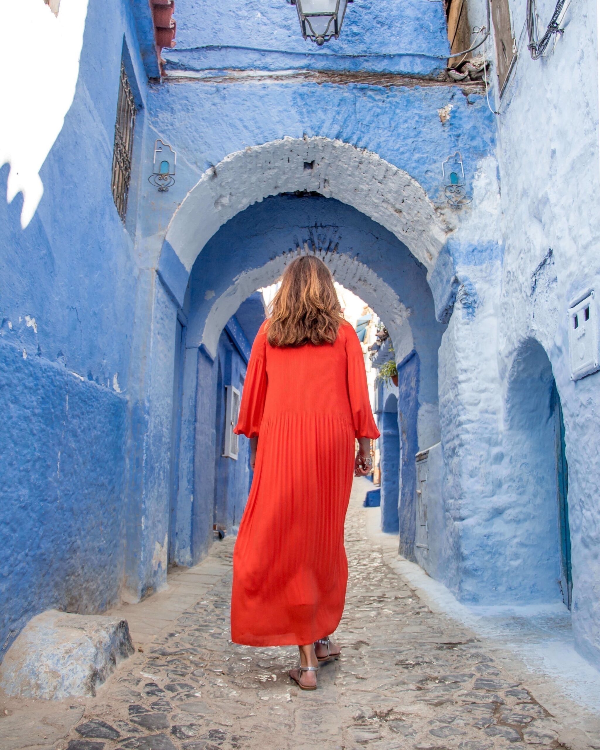 Chefchaouen - lady in red. Dame i rød kjole, en stor kontrast til de blå murhusene i den smale gaten damen går i. 