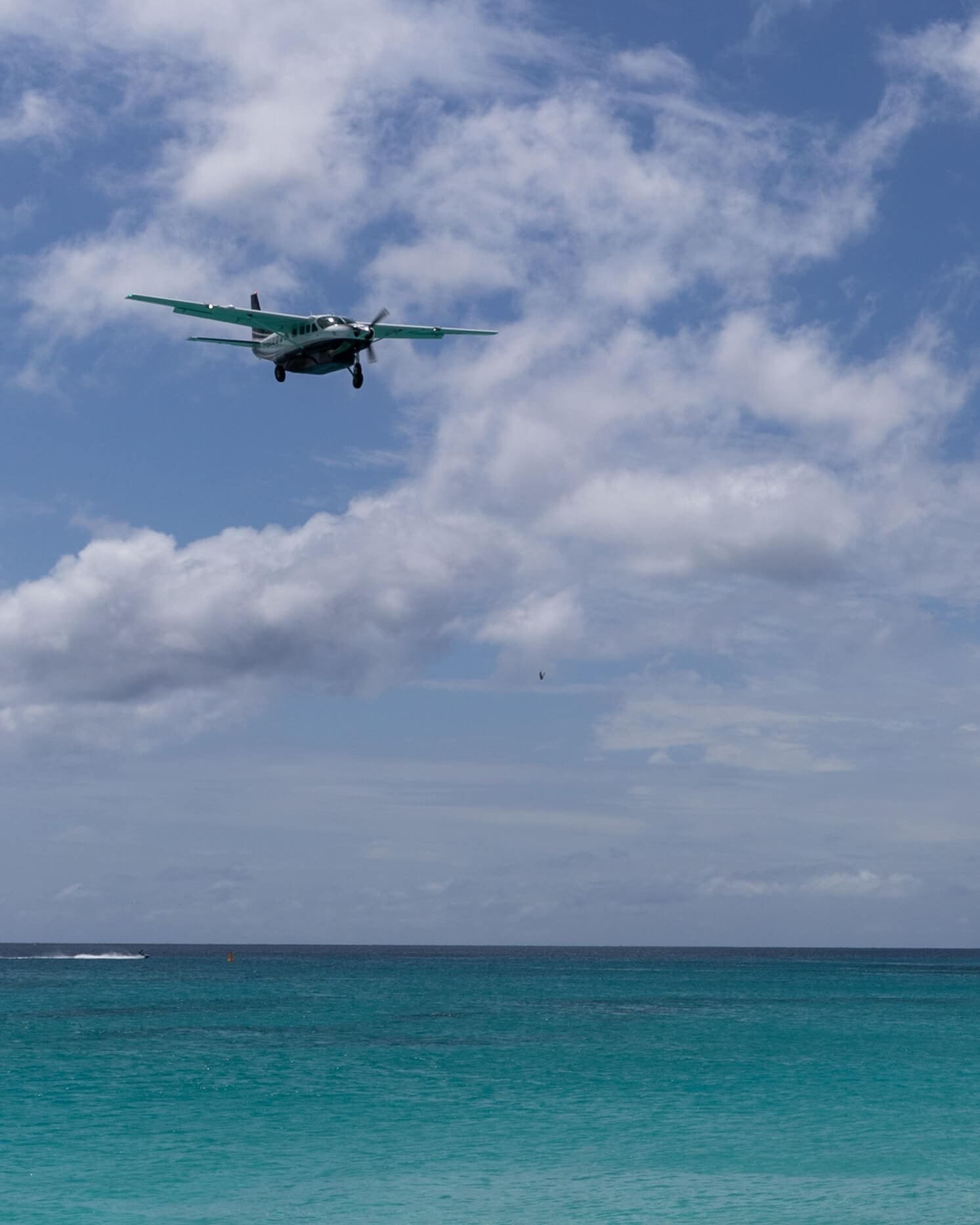 Et fly i luften sett fra strand på St Martin i Karibien. Flyet er lite, himmelen blå og havet turkist. 