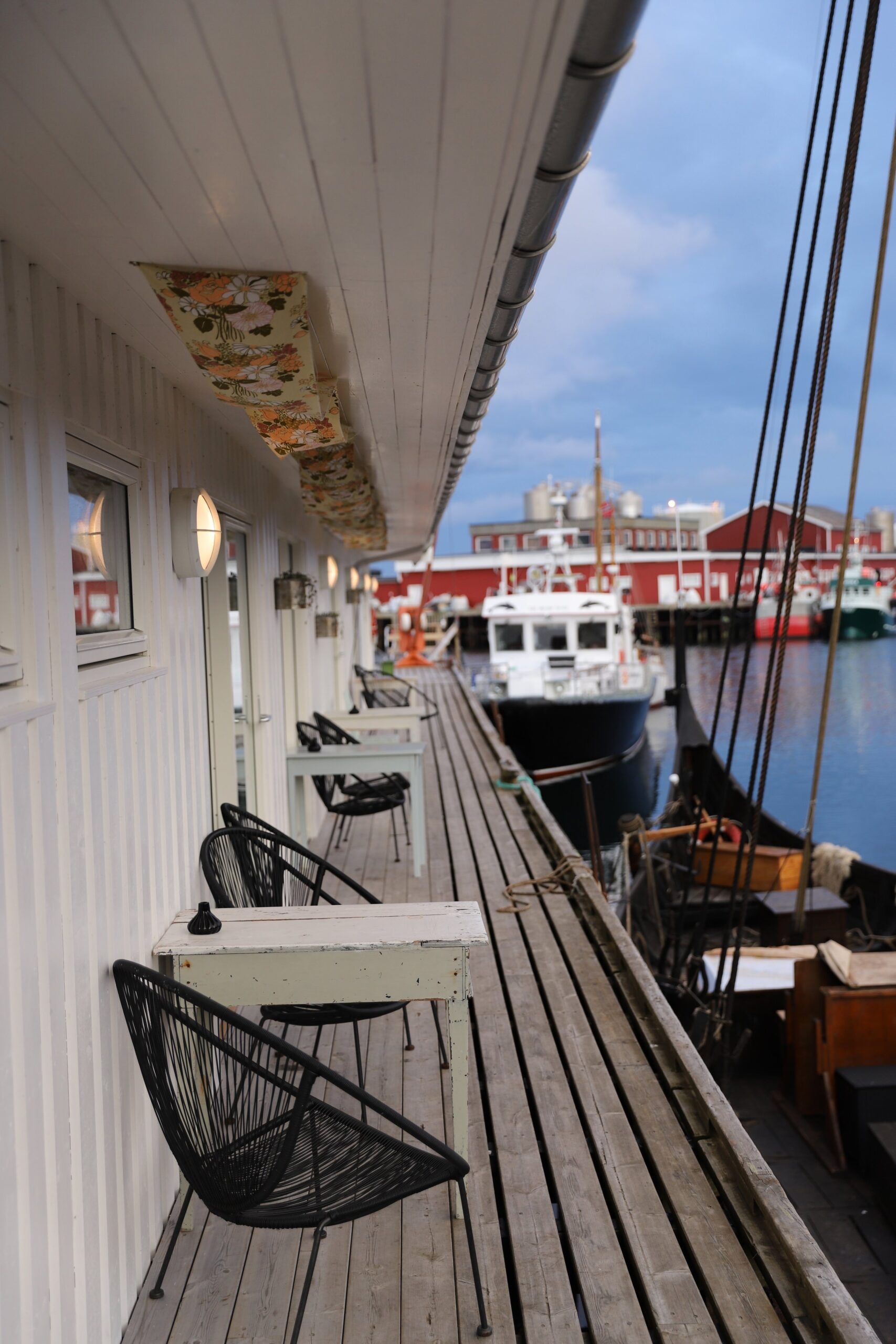 Lofoten Ballstad utsikt over havna og båter fra terrassen med bord og stoler ved Solsiden restaurant. 