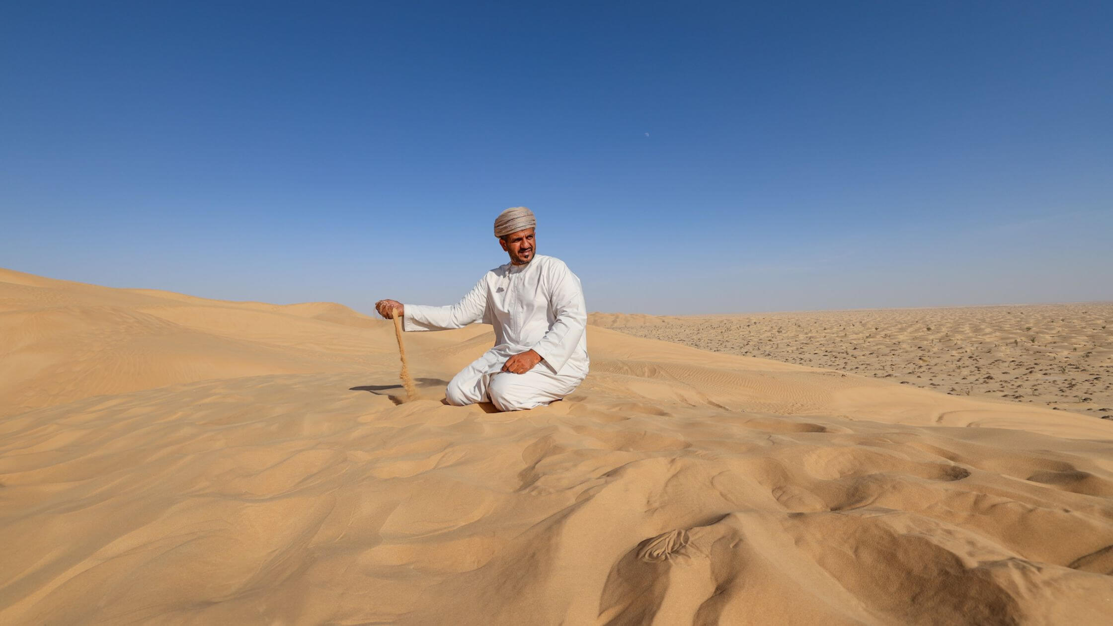 En araber I tradisjonell drakt sitter i sanden i Empty Quarter desert i Oman.