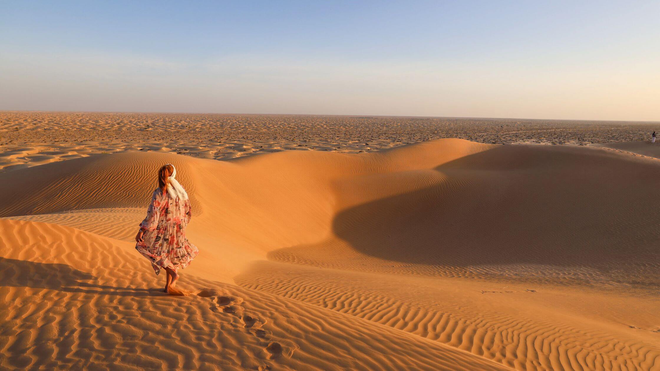Oman orken dame ikledd kjole i sanddynene ved solnedgang.