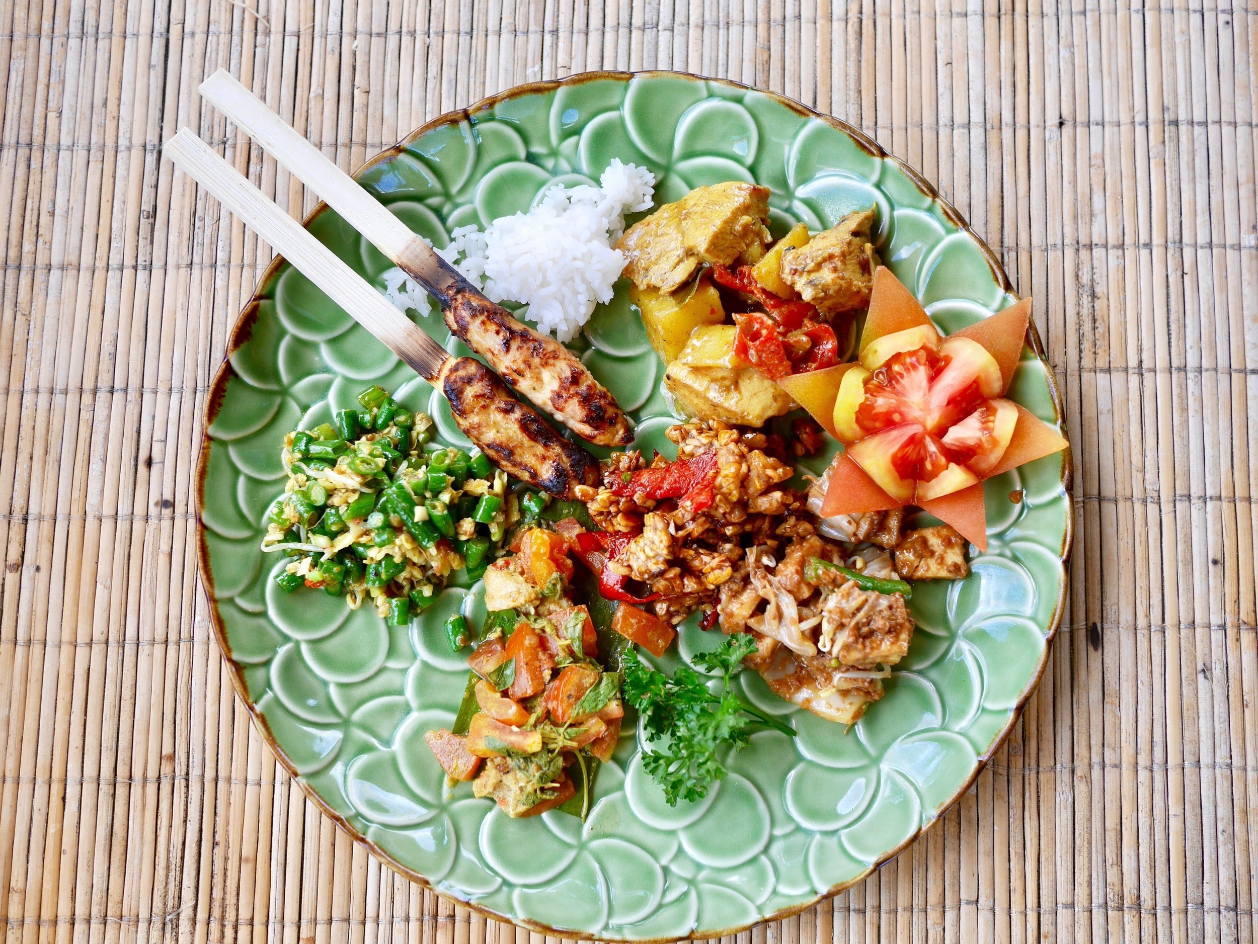 Bali cooking class sate siap with rice and vegetables on a green plate.