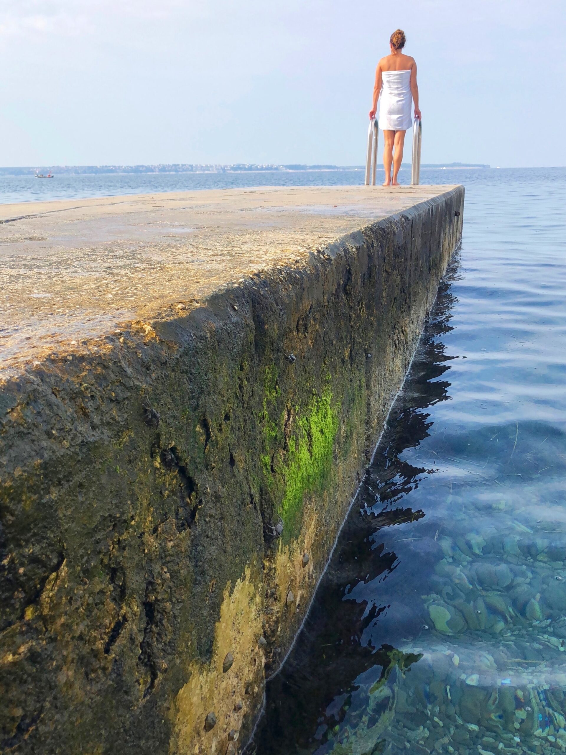 Badebrygge Piran Slovenia. Dame ved badetrapp med håndkle rundt seg og speider utover havet.