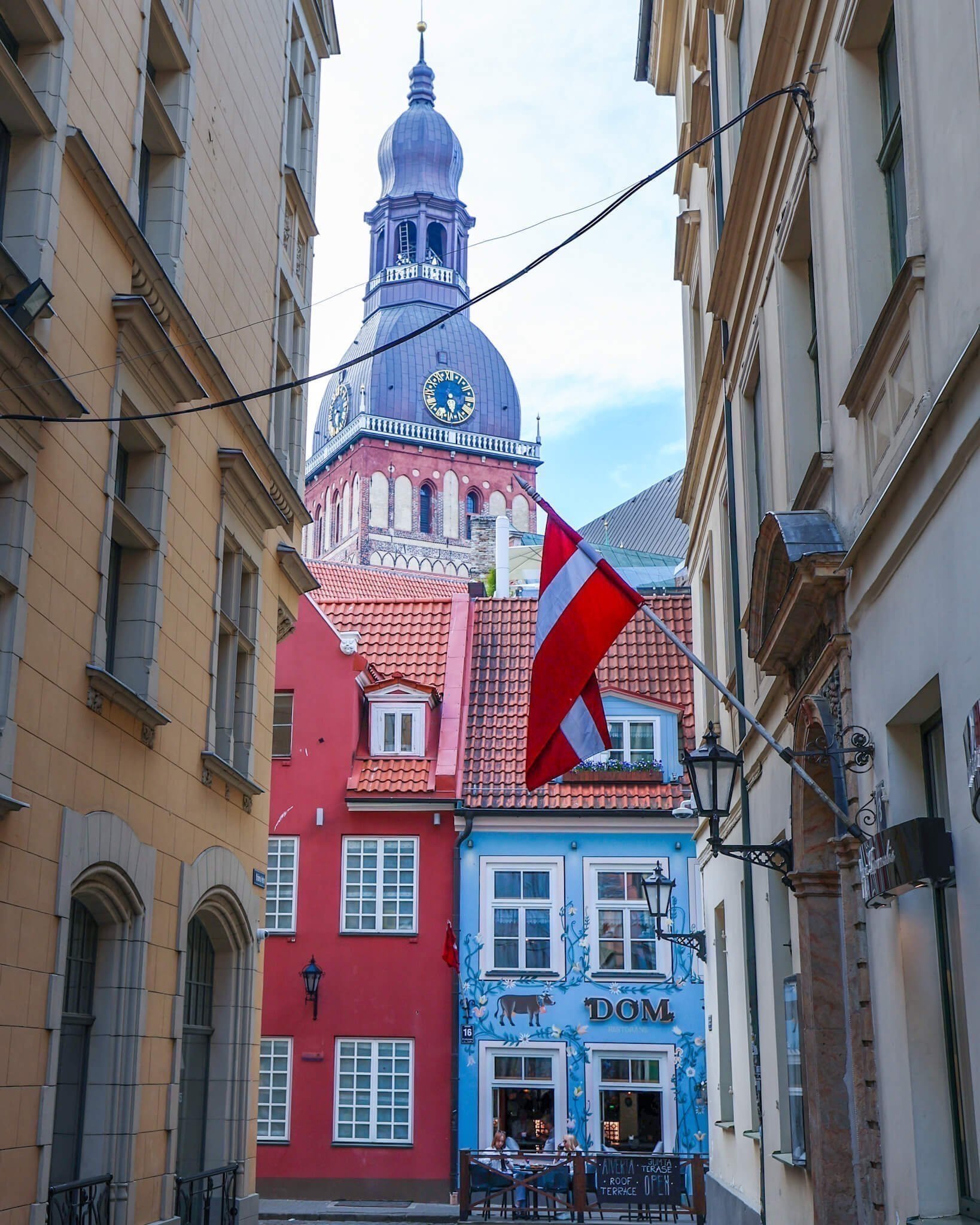 Gamlebyen står på UNESCOs verdensarvliste. I den sjarmerende gamlebyen i Latvias hovedstad er det brosteinsbelagte gater og historiske hus, mange av disse er nå omgjort til hyggelige restauranter og kaféer som disse to husene det røde og det blå som ligger ved kirken. 