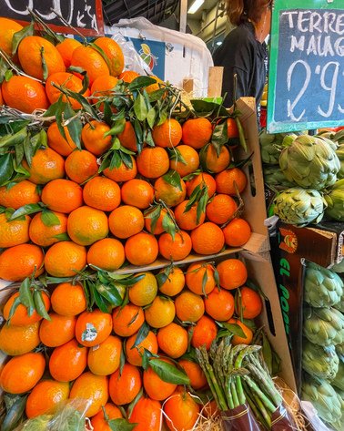 Grønnsaksmarked i Malaga. En kasse med orange solmodne appelsiner, asparges og artisjokker. 