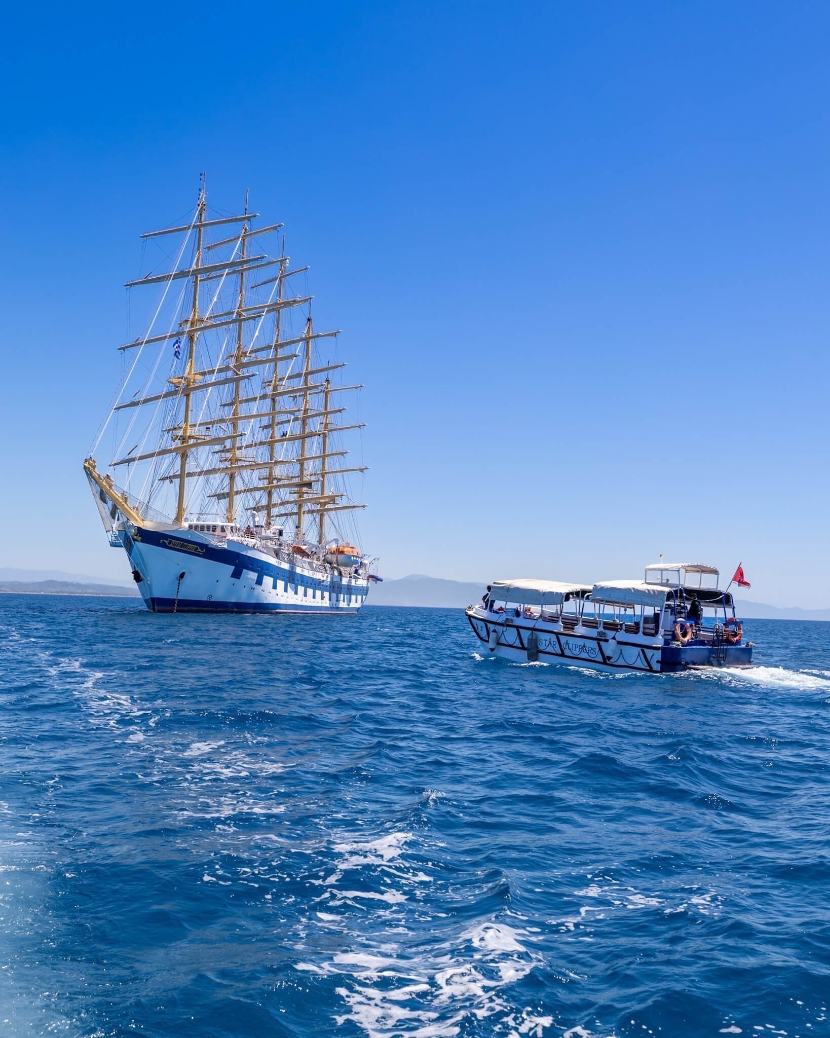 Seilskuten Royal Clipper uten seil. En mindre båt kjører passasjerer fra skuta til og fra land. 