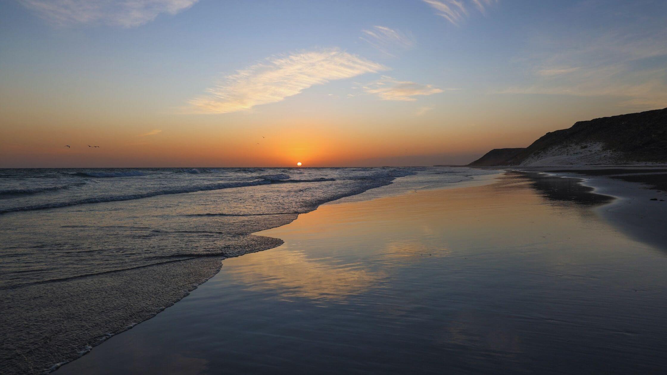 Vakker folketom strand i solnedgang og bølger som slår innover land.