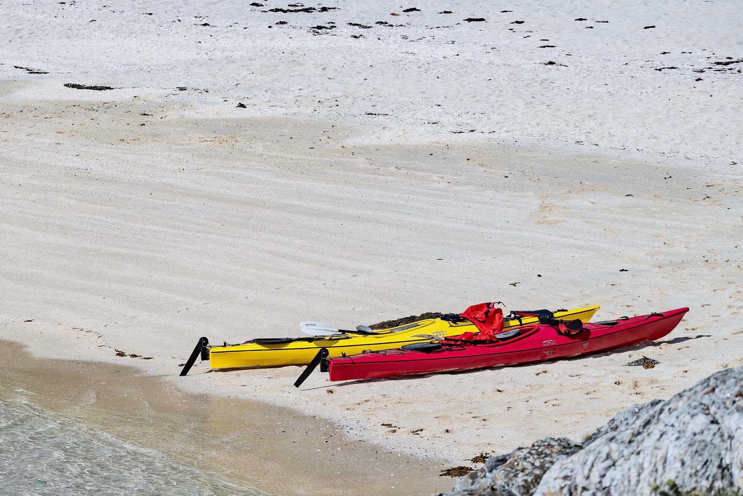 To kajakker, en gul og en rød, dratt opp på stranden på Sommarøy. 