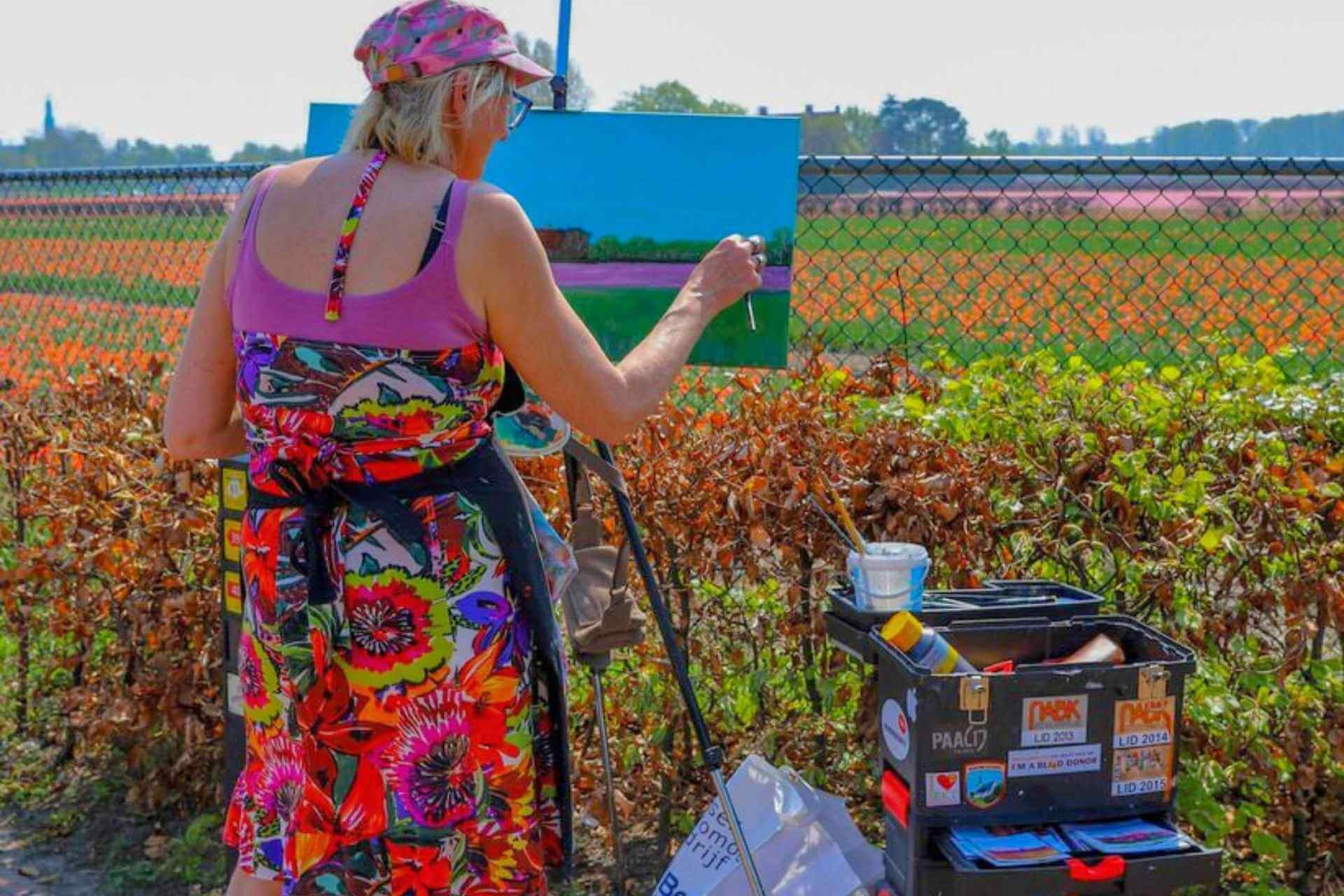 Dame med staffeli, sommerkjole og caps som maler ved tulipanfelt i Lisse i Nederland i tulipansesongen