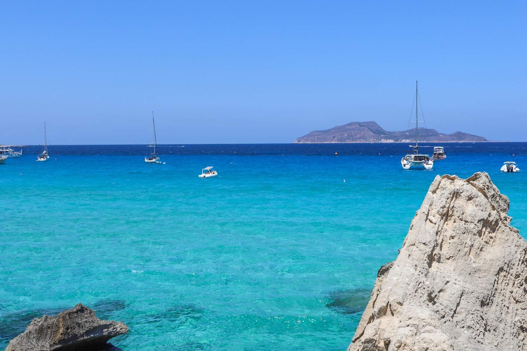 Krystallklart turkist vann p&aring; Favignana i Egadi&oslash;yene utenfor Sicilia med b&aring;ter og klippekyst