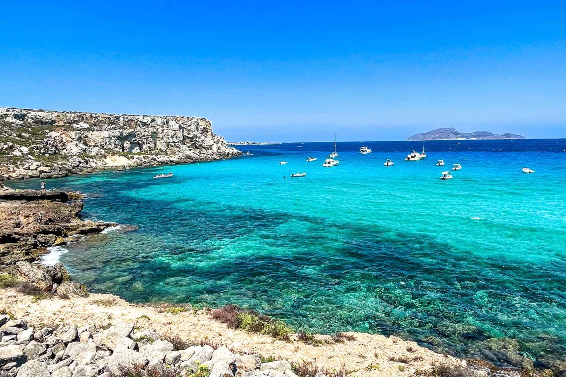 Strand p&aring; Favignana i Egadi&oslash;yene utenfor Sicilia med turkist vann og sm&aring;b&aring;ter i bukten