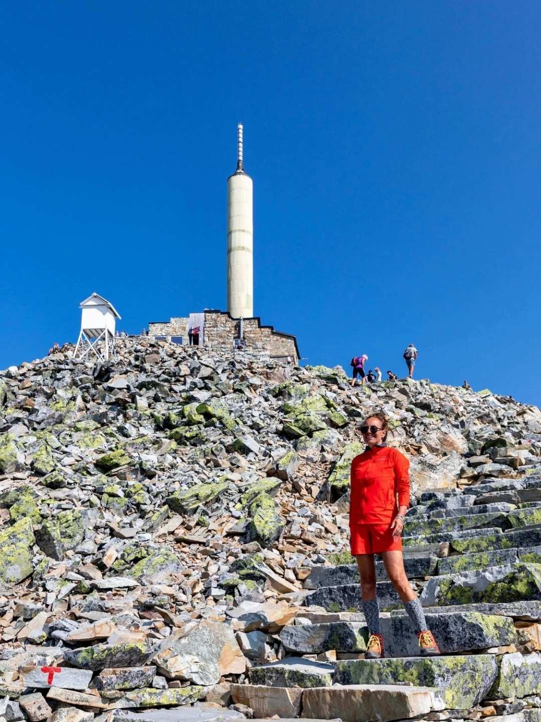 Dame kledd i rød short og rød jakke på toppen av Gaustatoppen.