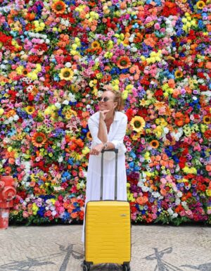 Gul kabinkoffert North Pioneer, dame og en vegg full av blomster.
