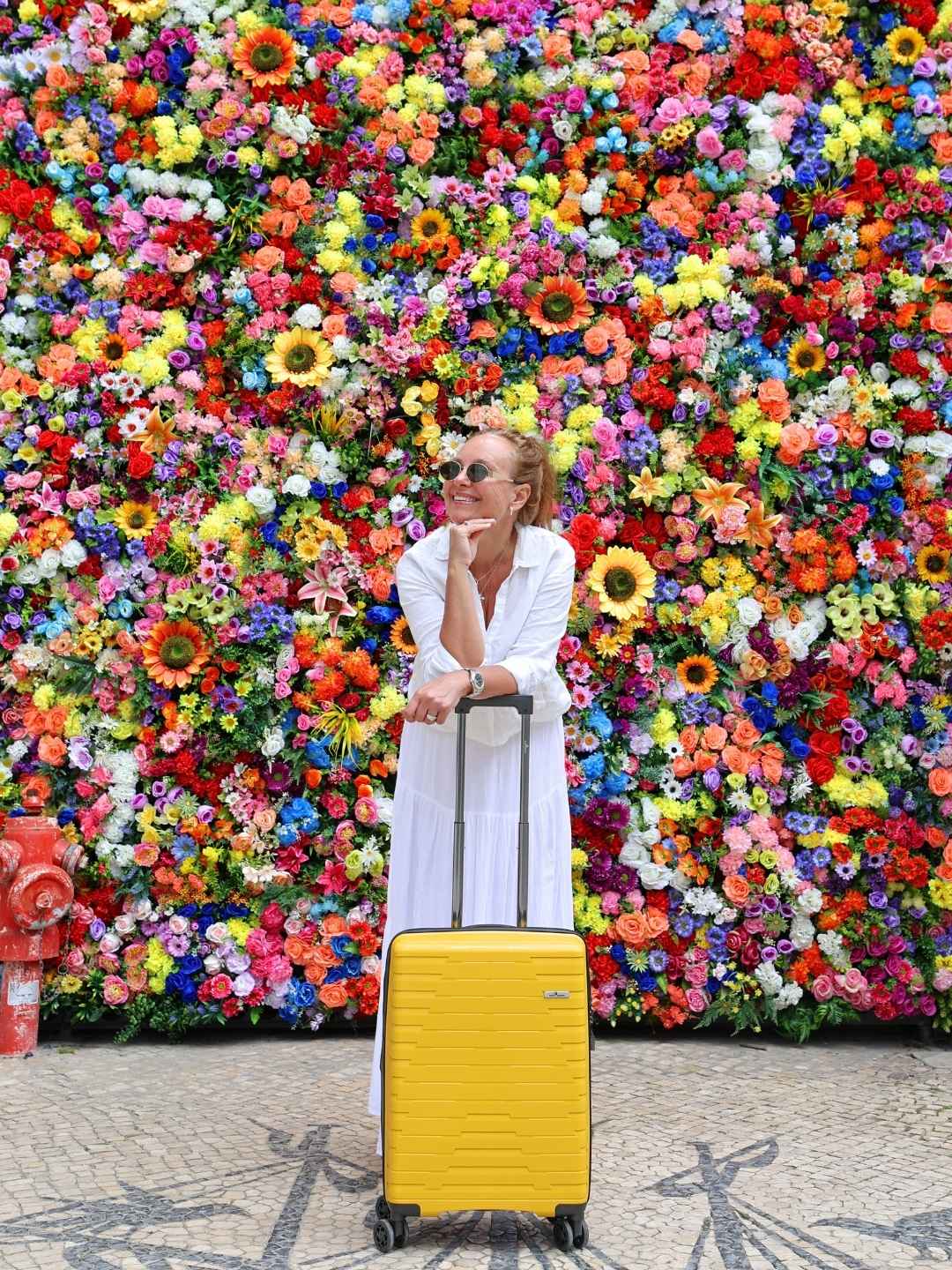 Gul kabinkoffert North Pioneer, dame og en vegg full av blomster.