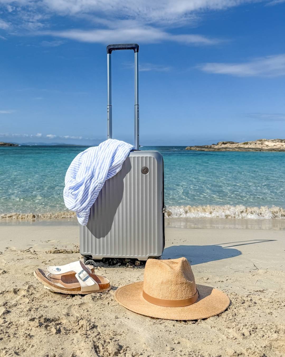 Kabinkoffert i lekker aluminiumspook på strand med turkist hav.