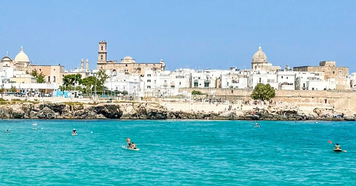 Gamlebyen i Monopoli med turkist hav med folk som bader på bystrand i forgrunden.