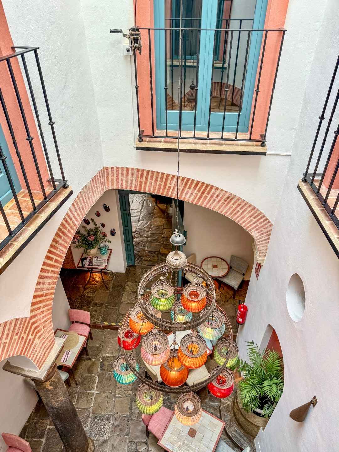 La Sacristia Tarifa atrium med stor lysekrone med fargede kupler og farger i interiør som plukker opp fargene fra lampen.