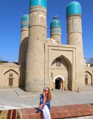 Merete Moen foran Chor Minor i Bukhara, Usbekistan – et ikonisk landemerke med fire blå kupler og utsmykninger som forteller historien om Silkeveien.