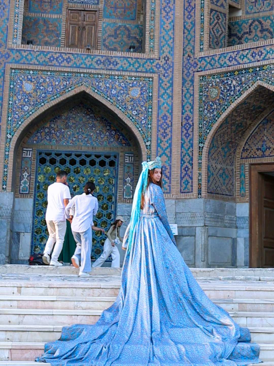 Dame i blå kjole foran mosaikkportalen i Shah-i-Zinda i Samarkand, Usbekistan – et hellig kompleks kjent for sine blå fliser og islamske kunst fra 1300-tallet.