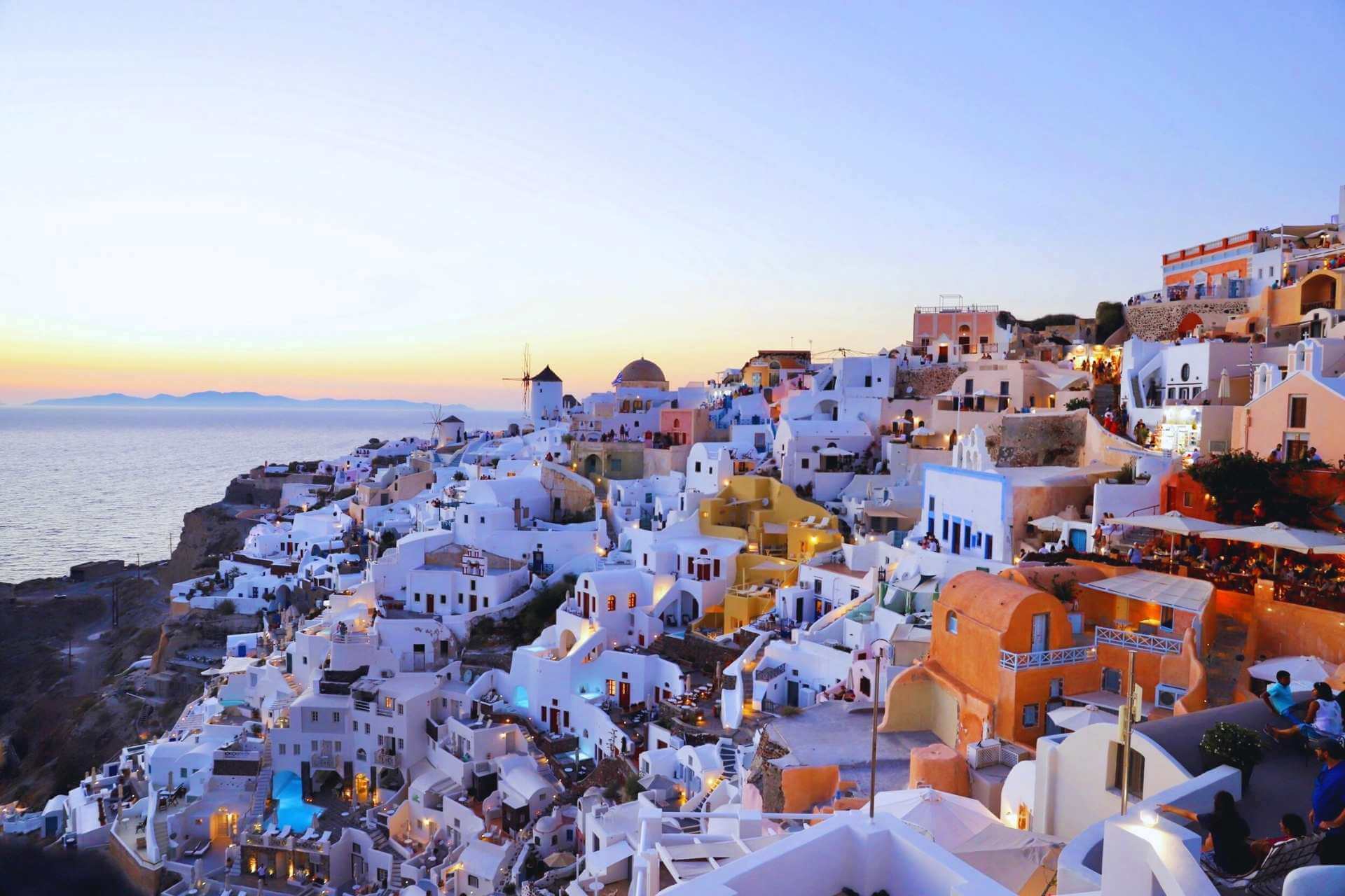 Solnedgang over hvite hus og klipper ved havet p&aring; Santorini i Kykladene, Hellas