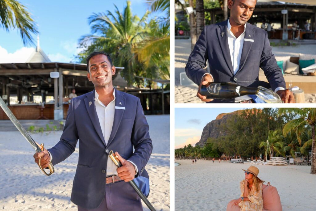 Sommelier ved St. Regis Le Morne utfører det ikoniske sabrage-ritualet på stranden med sabel og champagneflaske, omgitt av palmer og ettermiddagssol.