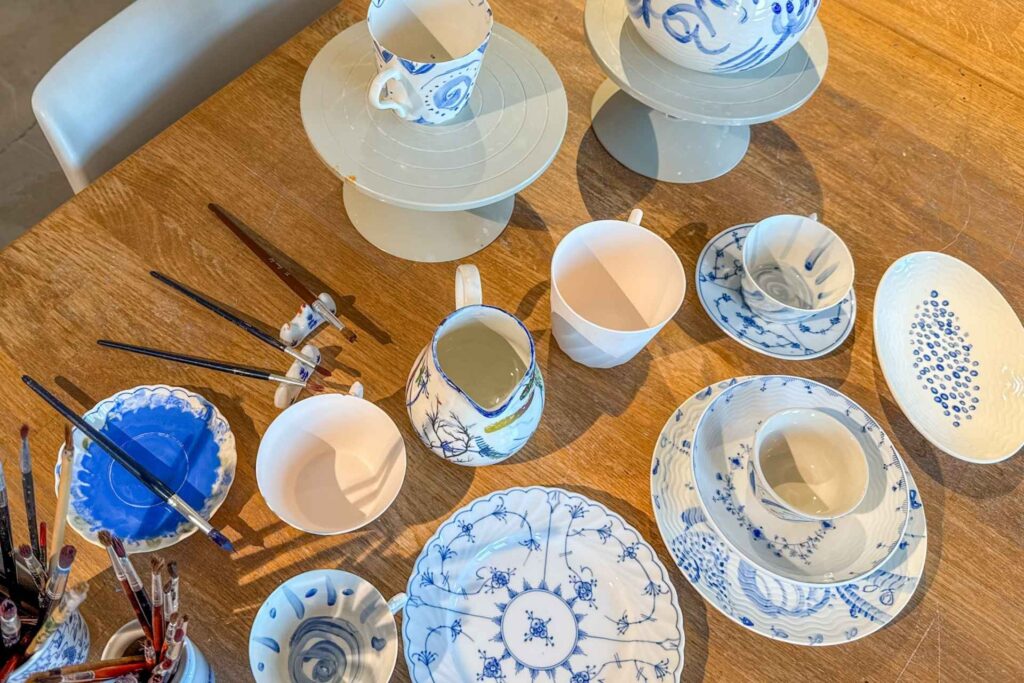Bord med porselenskopper, pensler og håndmalte kopper. Deler fra stråmønsteret synes også. 