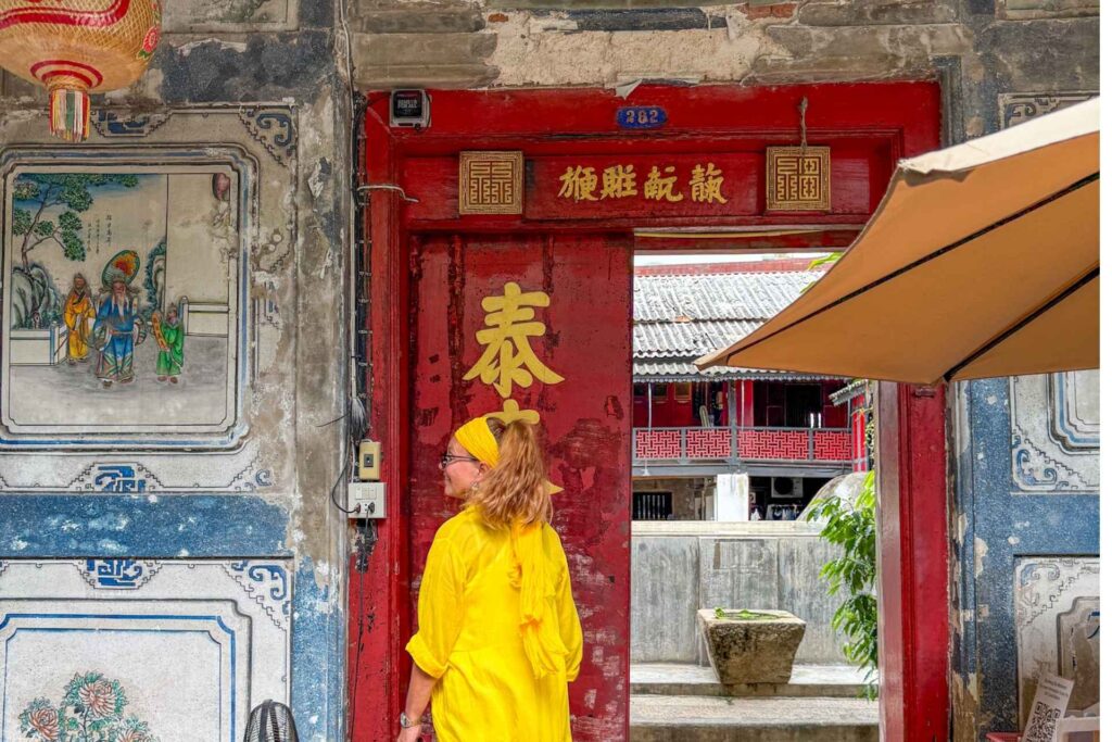 Kvinne kledd i gult g&aring;r inn historisk port i Bangkoks Chinatown med tradisjonell kinesisk arkitektur og slitte fasader.