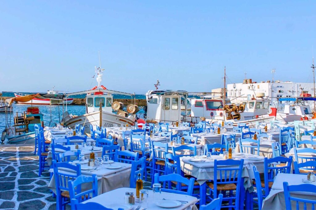 Havn i Naoussa p&aring; Paros i Hellas, med fiskeb&aring;ter og taverna-bord ved sj&oslash;en. 