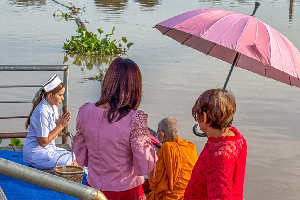 Tradisjonell morgengivning til munker ved elven i Uthai Thani, en viktig del av hverdagslivet i Thailand.