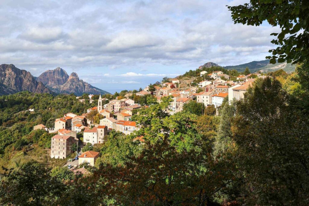Tradisjonell landsby i fjellene på Vest-Korsika omgitt av grønt landskap og dramatiske fjellformasjoner.