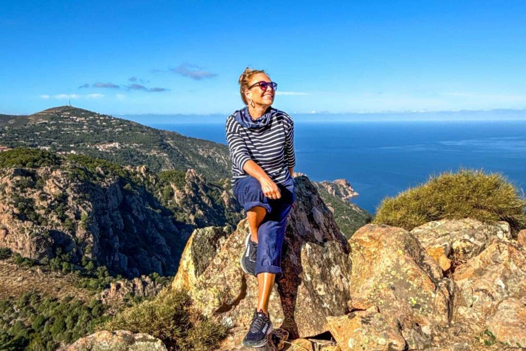 Turgåer sitter på en sten i forgrunnen med utsikt fra fjellene i Vest-Korsika over Middelhavet. Et populært område for fotturer og naturopplevelser.