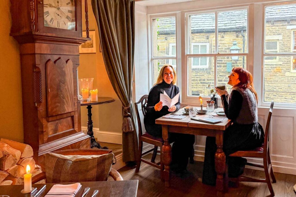Stemningsfullt spisested i Haworth med historisk interi&oslash;r og levende lys. To kvinner sitter ved et bord og drikker te. 